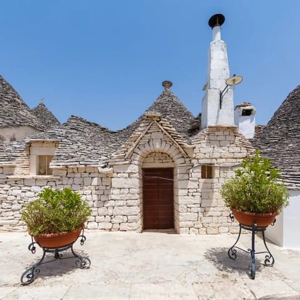 A picturesque view of traditional trulli houses in Puglia, Italy, featuring their distinctive conical stone roofs and white-washed walls under a clear blue sky, with potted plants in the foreground.