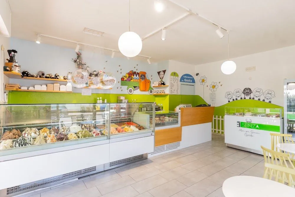 An interior view of a brightly lit and clean ice cream or gelato shop. The image features display cases filled with various colorful gelato flavors, along with whimsical wall art depicting a fruit truck and sheep. The space is well-maintained with light-colored flooring and modern lighting fixtures.