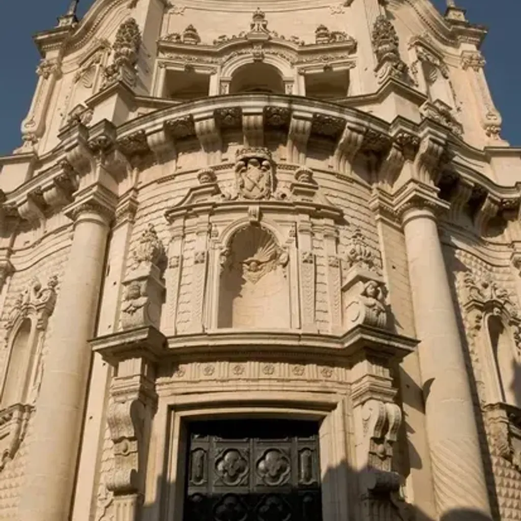 An image capturing the ornate facade of an old, intricate stone building, possibly a church, under natural sunlight. The detailed carvings and architectural elements are prominent.