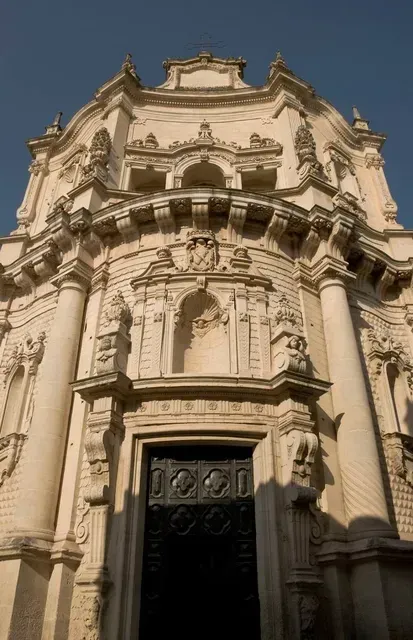 An image capturing the ornate facade of an old, intricate stone building, possibly a church, under natural sunlight. The detailed carvings and architectural elements are prominent.