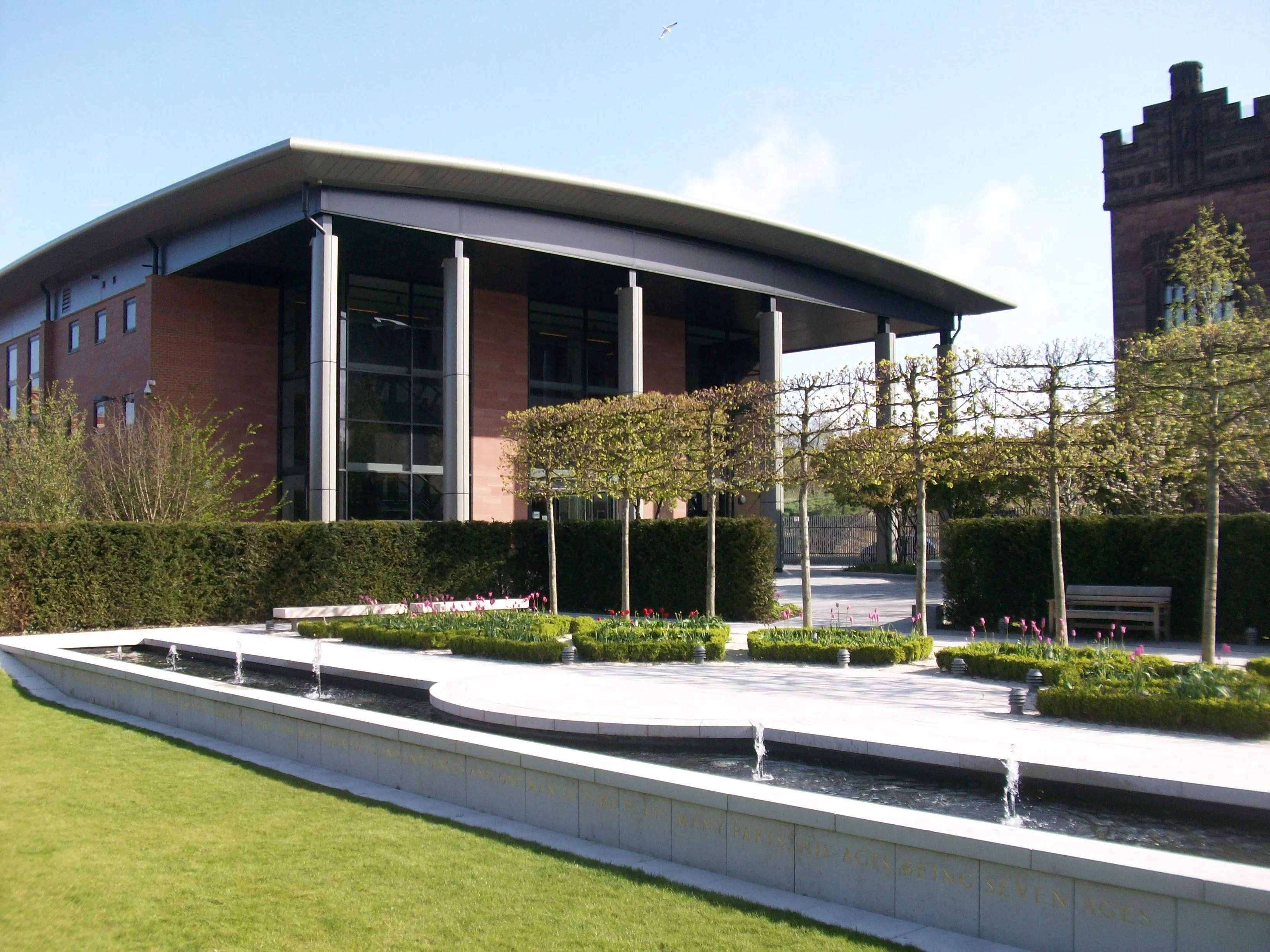 The image is well-lit, sharp, and photo-realistic with accurate colors. Key elements like the modern building, garden, and water feature are all in clear focus. The composition is generally good, showcasing the architectural and landscape elements effectively. A slightly more dynamic angle might have enhanced the architectural features further.