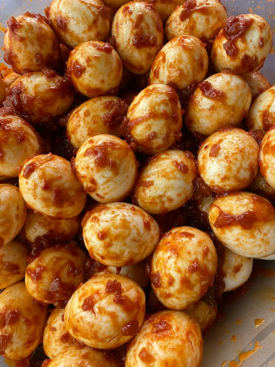 A close-up shot of numerous small, peeled eggs coated in a rich, reddish-brown sauce.