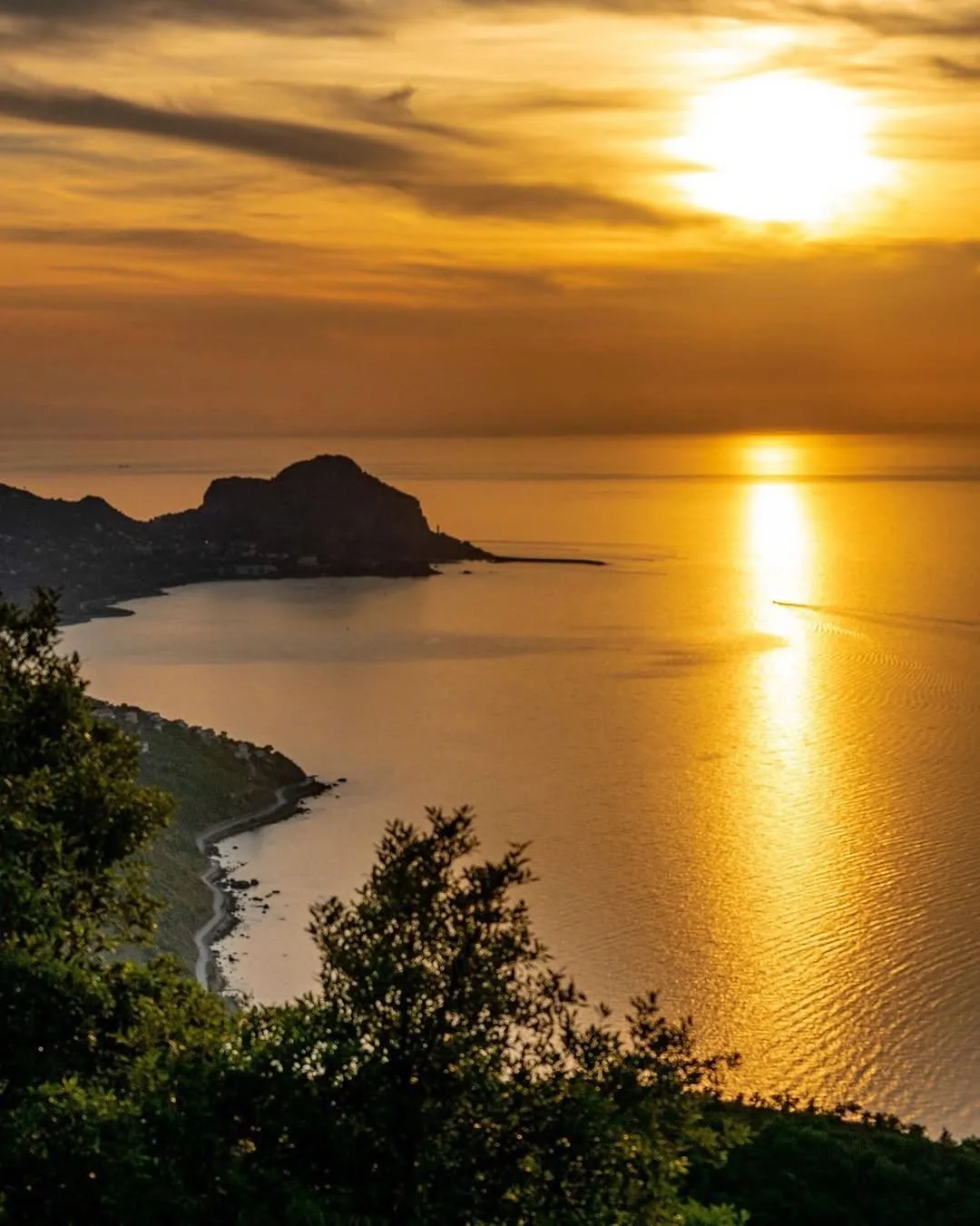 A beautiful and well-composed landscape image capturing a sunset or sunrise over a body of water with a prominent landmass. The golden light creates a stunning reflection on the water.