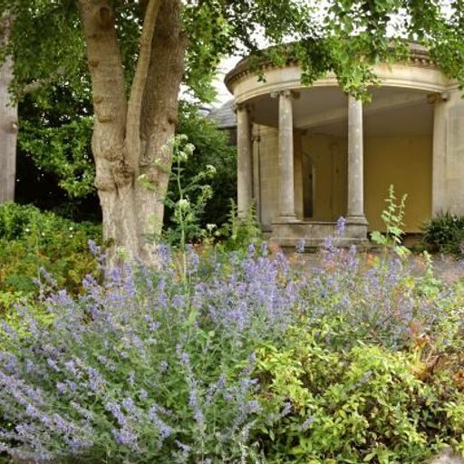 This image is well-composed, showing a pleasing arrangement of garden elements. The lighting is good, creating a natural and even exposure. The image is sharp, with details in the plants and stonework clearly visible. Colors are accurate and natural-looking. The photo has a photorealistic quality, conveying a sense of place and atmosphere. Key elements, such as the gazebo and flowers, are in focus. The overall quality is high, resulting in a visually appealing image. No unwanted elements are present.