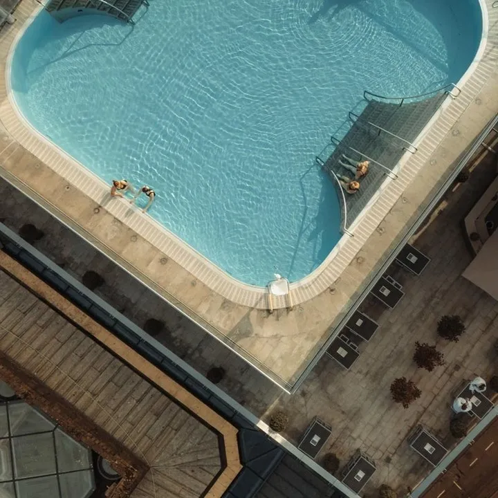 An aerial view of a swimming pool, showcasing its clean blue water and the surrounding concrete structures under natural sunlight. The image is well-composed with clear lines and good lighting, and appears sharp and photo-realistic.