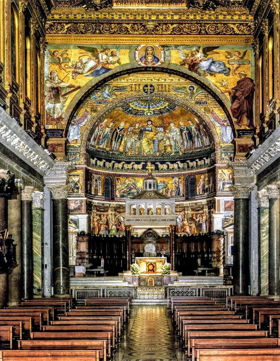 A stunning interior view of a historic church, showcasing intricate gold mosaics and ornate architectural details. The image features rows of wooden pews leading towards a beautifully decorated altar and apse, all under the grandeur of the mosaic artwork.