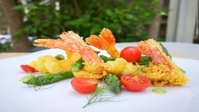 The image is a well-lit and photo-realistic depiction of a food dish featuring fried shrimp, asparagus, and cherry tomatoes. The colors are vibrant and appear accurate, enhancing the appeal of the meal. The main subjects are sharp and in focus with a pleasant shallow depth of field that blurs the background.