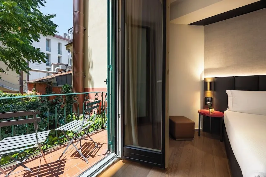 The image is well-composed, using the doorway to frame both the balcony and the adjacent room, showcasing a balanced view of both spaces. It is sharp with good detail evident in both foreground and background elements. Colors appear natural and accurate. The image is highly photo-realistic, and key elements in both the indoor and outdoor areas are clearly in focus. The lighting is generally good, effectively illuminating both the sunlit balcony and the interior.