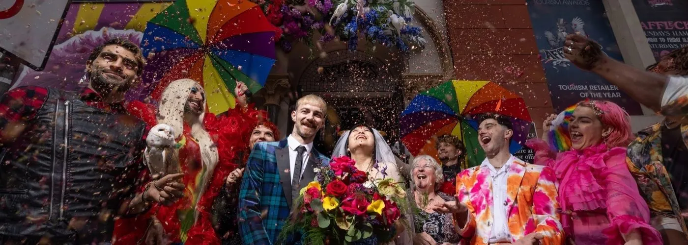 A vibrant and joyful editorial-style image capturing a couple celebrating under a shower of confetti, surrounded by colorful umbrellas and flowers.