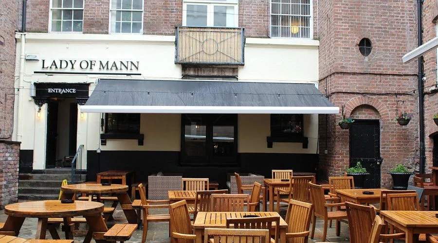 The image is photo-realistic, capturing an outdoor seating area of a venue effectively. The key elements, including the wooden tables and chairs, are sharp and in focus. The colors appear accurate and natural for the scene. The lighting is somewhat flat due to overcast conditions, which reduces visual dynamism. The composition is decent, providing a clear view of the area.
