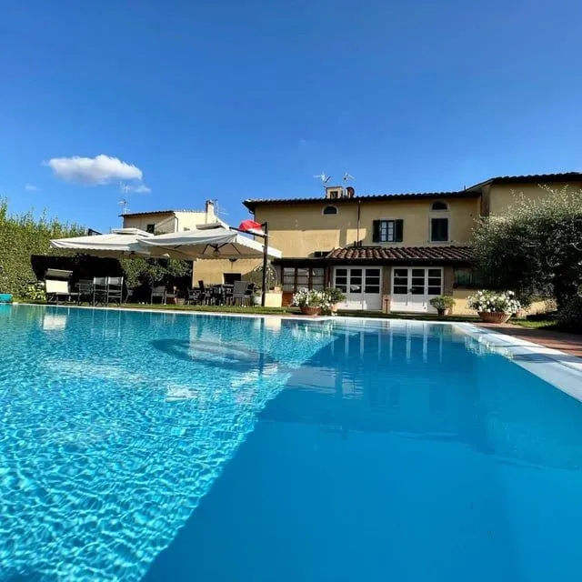 The image is very well-lit, capturing a bright and inviting scene under clear blue skies. The colors are vibrant and accurate, especially the deep blue of the pool and the warm tones of the building. Sharpness is excellent throughout, with both the pool and the background building appearing crisp and detailed. The composition effectively frames the beautiful property, although the foreground pool takes up a significant portion of the frame. All key elements are in focus, contributing to a highly photo-realistic and appealing image.