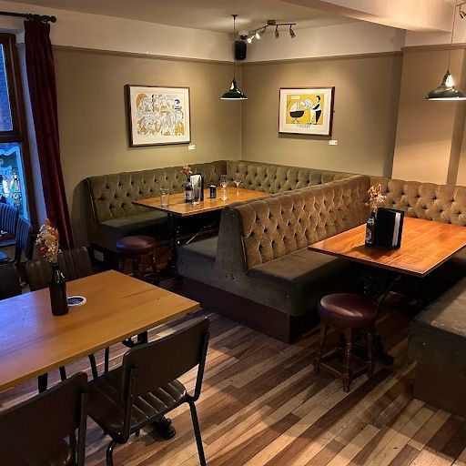 This image captures the interior of a restaurant, showcasing booth seating, tables, and chairs. The composition is well-balanced, with the focus on the seating arrangements and the wooden floor. The lighting is warm and inviting, creating a pleasant atmosphere. The image is sharp, with good detail in the furniture and artwork. The color accuracy is excellent, with natural-looking tones. The image is photo-realistic, capturing the space accurately. There are no unwanted elements present, such as selfies, promotional graphics, or cluttered environments. The image is a good representation of the interior space and effectively conveys the ambiance of the restaurant. The image could be slightly improved by focusing on a specific aspect of the interior, such as a particular booth or table, to create a more compelling visual. Overall, the image is well-composed and well-lit, with a high level of detail and color accuracy. It is a good example of interior photography for a restaurant.