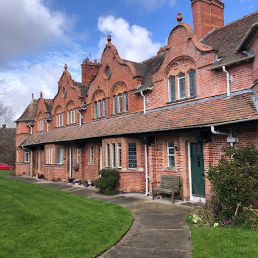 This image is a well-composed exterior shot of a row of brick buildings. The composition is balanced, with the buildings taking up a significant portion of the frame and the lawn and path providing a sense of depth. The lighting is natural and well-balanced, showcasing the details of the brickwork and the windows. The image is sharp, with good detail throughout. The colors are accurate and pleasing, with a warm, earthy tone. The key elements, such as the buildings, windows, and door, are in focus. The image is free of unwanted elements, such as selfies, promotional graphics, advertisements, or cluttered environments. Overall, this is a high-quality image that effectively captures the architectural details and aesthetic appeal of the subject.