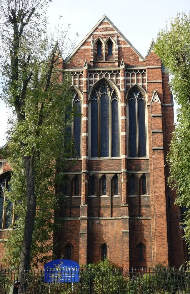 The image showcases the intricate architectural details of a brick building, likely a church or historical structure, framed by green trees. It is well-lit, sharp, and photo-realistic, with accurate colors. The main architectural elements are clearly in focus. The composition is generally good, though the trees slightly obscure parts of the building.