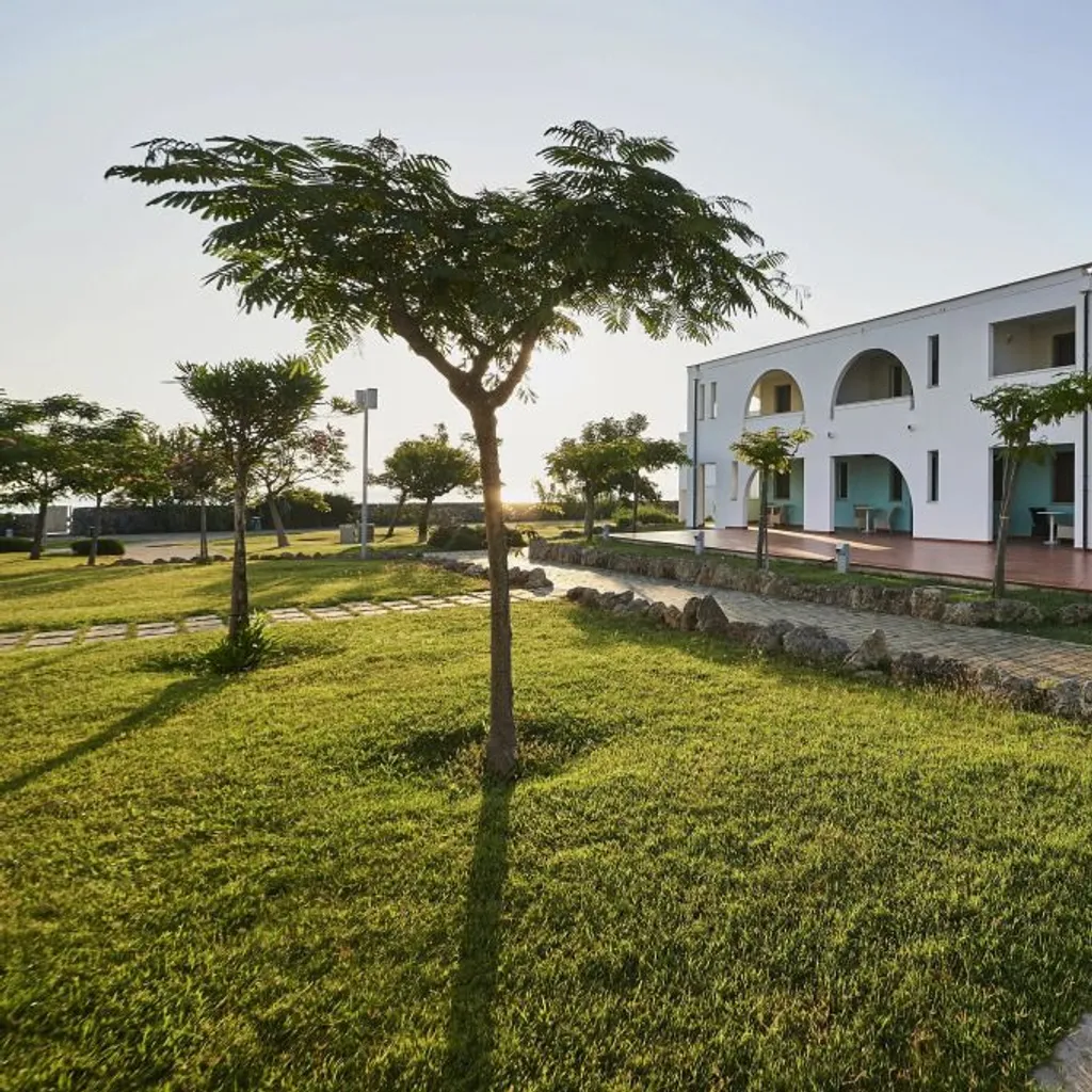 The image is photo-realistic, sharp, and generally well-lit with accurate colors. Key elements like the building and pathway are in focus. The composition is decent, though the foreground grass is quite dominant. The bright lighting on the white building might cause some slight highlight clipping.