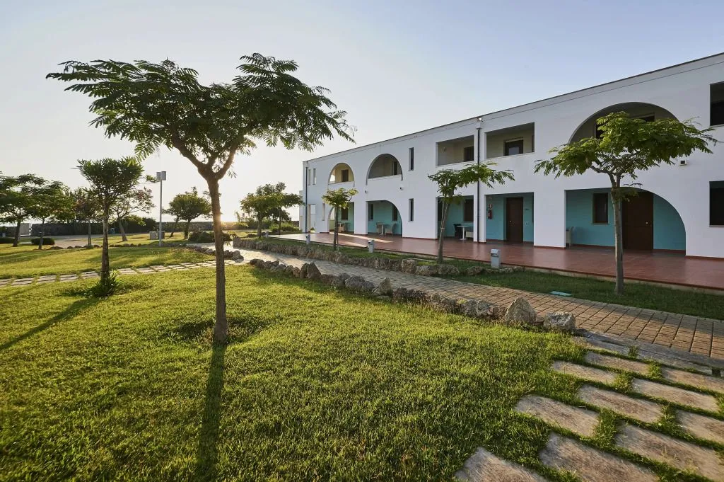 The image is photo-realistic, sharp, and generally well-lit with accurate colors. Key elements like the building and pathway are in focus. The composition is decent, though the foreground grass is quite dominant. The bright lighting on the white building might cause some slight highlight clipping.