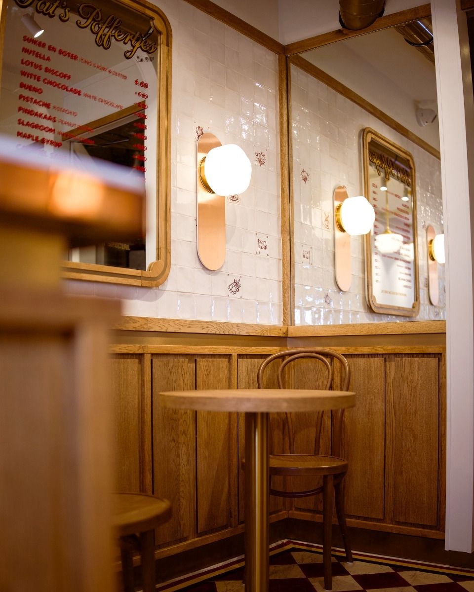 This image is a well-composed and well-lit shot of a restaurant interior. The composition is balanced, with the table and chairs positioned in the corner of the room, creating a sense of depth and perspective. The lighting is soft and even, highlighting the warm tones of the wood and tile. The image is sharp, with clear details visible in the wood grain, the tile patterns, and the reflections in the mirror. The colors are accurate and natural, creating a pleasant and inviting atmosphere. The key elements, including the table, chairs, and light fixtures, are all in focus. Overall, this image is a great example of professional interior photography, showcasing the restaurant's design and ambiance in a visually appealing way.