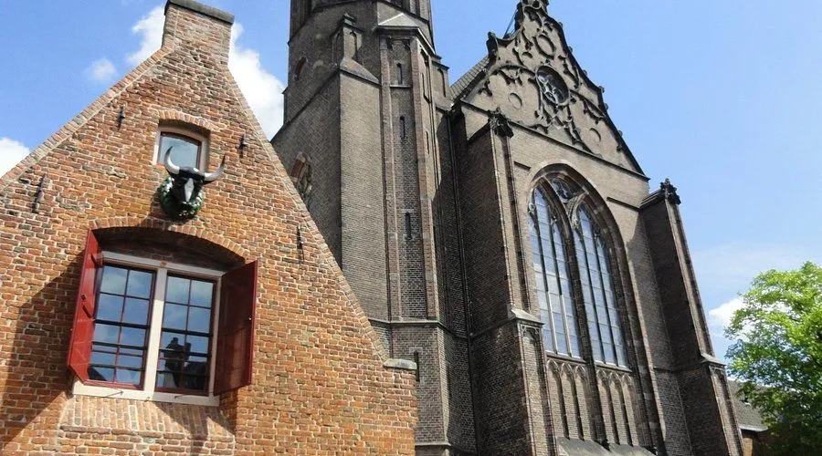 An eye-level shot capturing the intricate details of a historic brick church or large building with an attached, older brick house in the foreground. The sky is visible in the upper left, suggesting an urban or town setting.