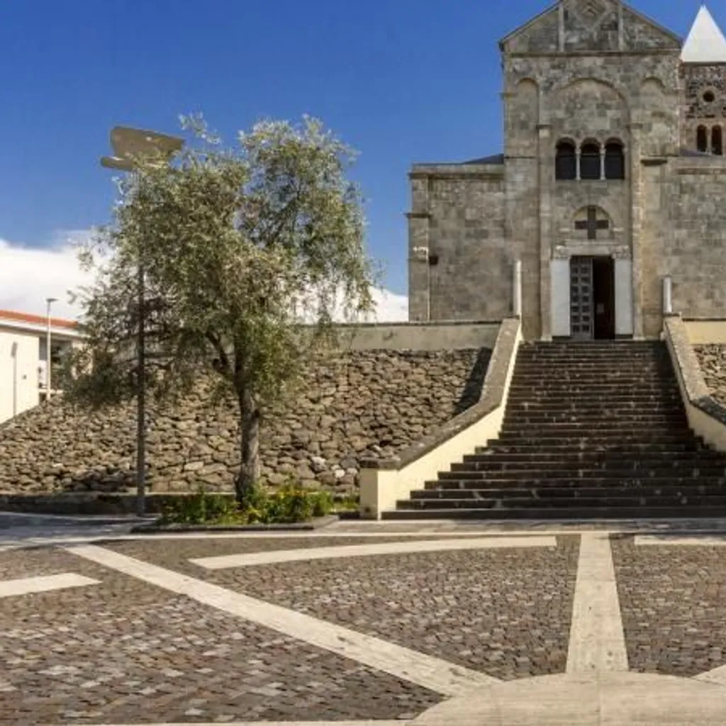 The image is well-composed, using leading lines from the patterned ground and long staircase to direct the eye towards the central church structure. It is well-lit by natural sunlight, ensuring good exposure and accurate color rendition, particularly for the blue sky and stone building. The image is sharp throughout, with strong photo-realism and all key elements, including the intricate details of the church facade and the foreground paving, clearly in focus.
