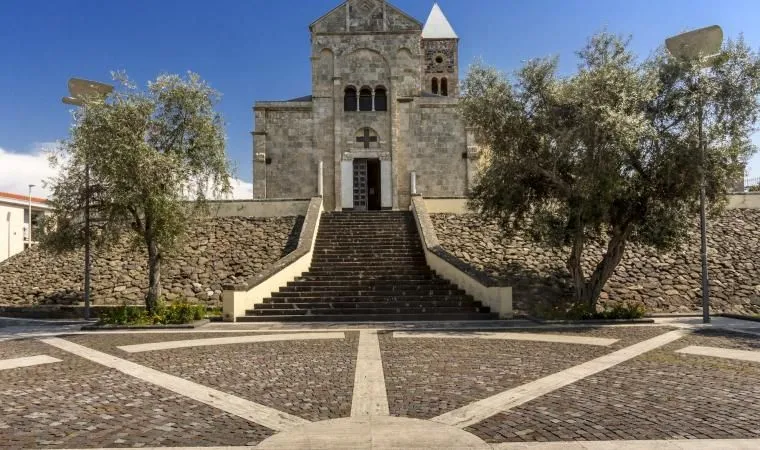 The image is well-composed, using leading lines from the patterned ground and long staircase to direct the eye towards the central church structure. It is well-lit by natural sunlight, ensuring good exposure and accurate color rendition, particularly for the blue sky and stone building. The image is sharp throughout, with strong photo-realism and all key elements, including the intricate details of the church facade and the foreground paving, clearly in focus.
