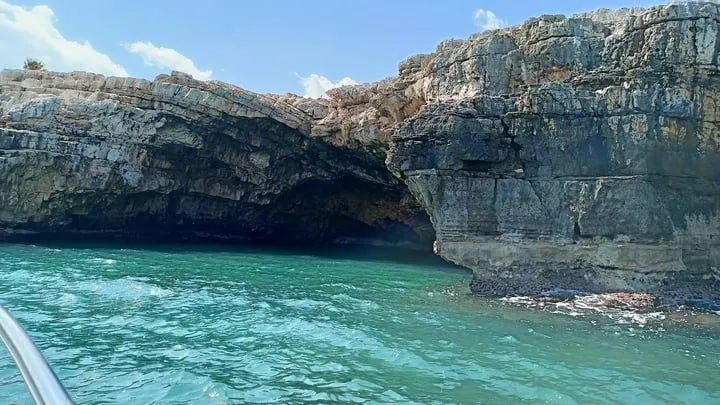 An editorial style image featuring a beautiful natural sea cave formation with clear, vibrant turquoise water under a blue sky.