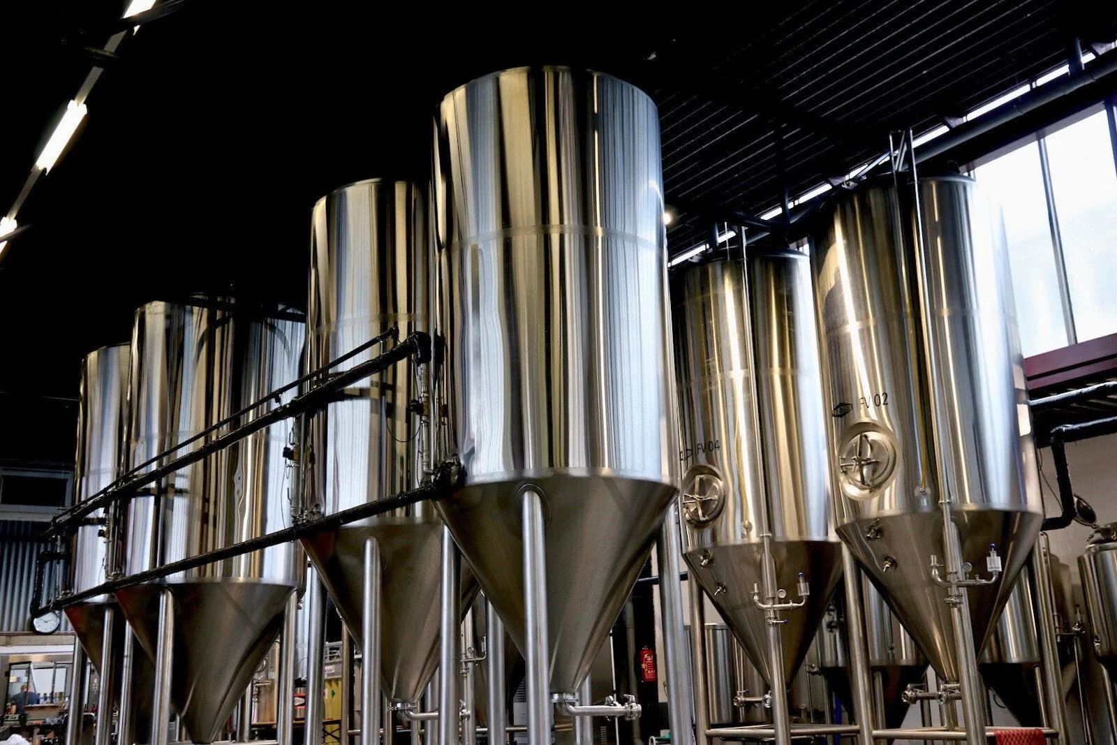 The image showcases several large, reflective stainless steel fermentation tanks within an industrial setting. It is well-composed with a dynamic perspective, emphasizing the scale and clean lines of the equipment. The lighting is effective, highlighting the metallic sheen and details without harsh shadows or overexposure. The image is sharp and photo-realistic, with all key elements in focus, contributing to its professional and clear appearance. The color rendition appears accurate for the subject matter.