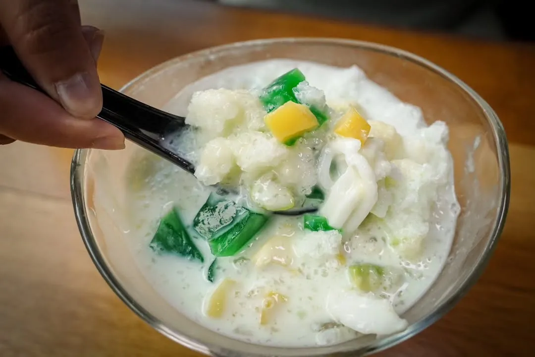 A vibrant and well-composed close-up shot of a milky shaved ice dessert with colorful jellies and other toppings. A spoon is seen scooping a portion, adding a dynamic element to the image.