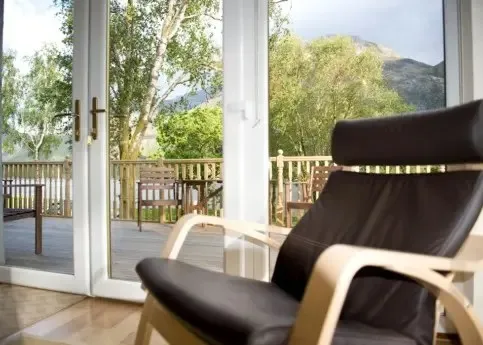 The image provides a clear view from an indoor space to an outdoor deck with a natural landscape. The lighting is natural and well-balanced, contributing to vibrant and accurate colors. The primary subjects, including the foreground chair and the deck, are in focus, though the distant background elements like the mountains appear softer.