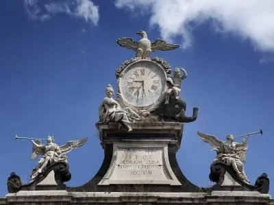 A well-composed, well-lit, and sharp photograph of an ornate clock and statues against a clear blue sky. The image is highly photo-realistic with accurate colors and all key elements in focus.