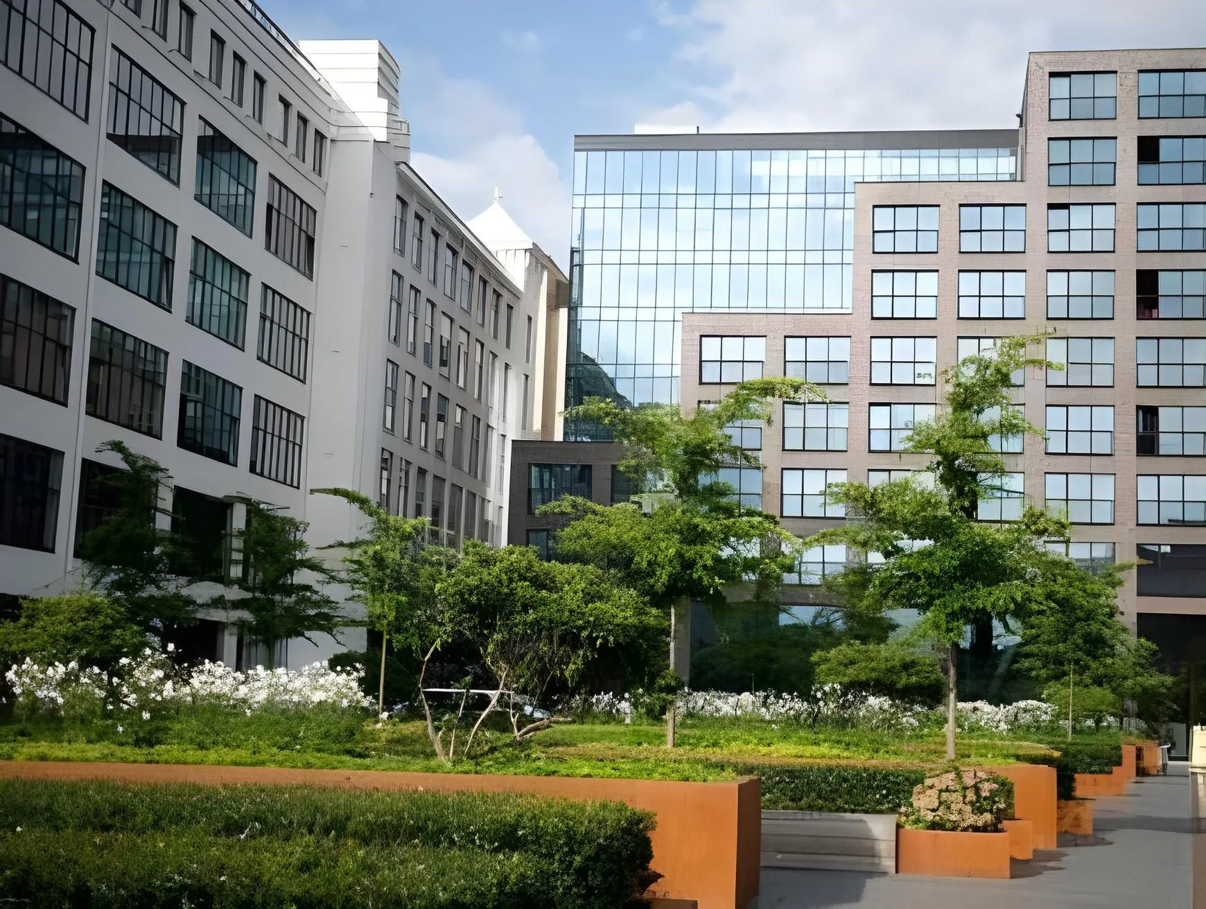 The image is a well-composed and sharp representation of modern architecture integrated with a landscaped green space. It benefits from natural, even lighting and accurate colors, contributing to its high photo-realism. Key elements, including both the buildings and the foreground greenery, are clearly in focus, making it a strong editorial-style image.