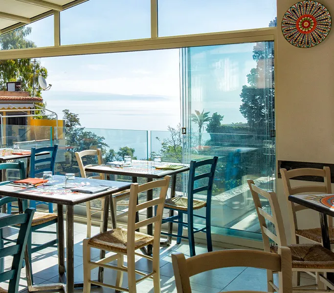 An inviting restaurant interior with a panoramic sea view, featuring well-arranged tables and chairs in natural light.