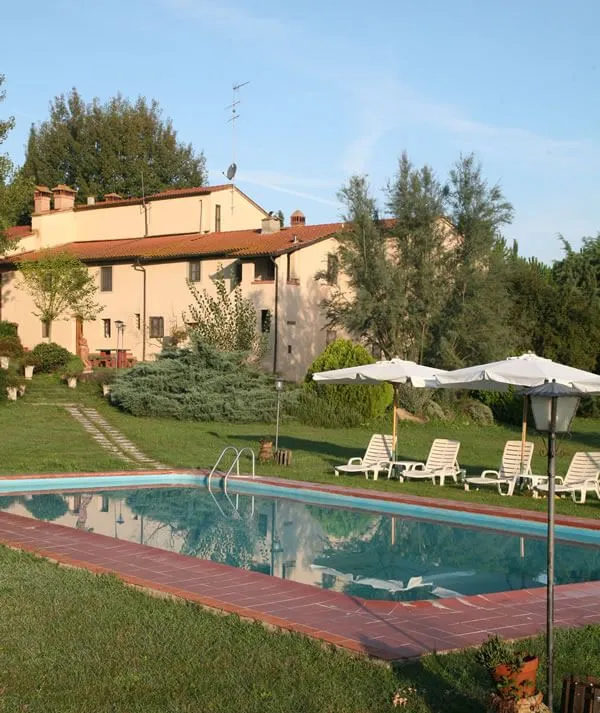 An inviting and well-lit image of a property with a swimming pool and lush green surroundings under a clear sky. The scene conveys a sense of tranquility and leisure.