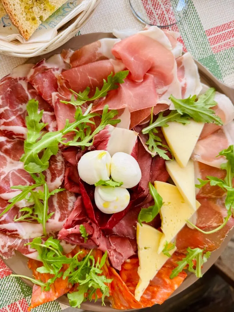 An overhead shot of a well-arranged charcuterie board featuring a variety of cured meats, cheeses, and fresh arugula.