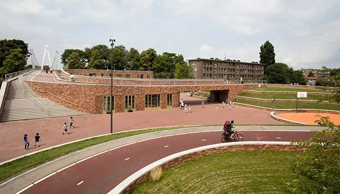 This is a well-composed and photo-realistic image showcasing an urban public space. The composition effectively uses leading lines from the bike path, guiding the viewer's eye through the scene. The natural daylight provides even illumination, and the colors are accurate. Key elements such as the architecture, bike path, and the cyclist are all sharp and in focus. The image successfully captures the essence of a modern, active public area.