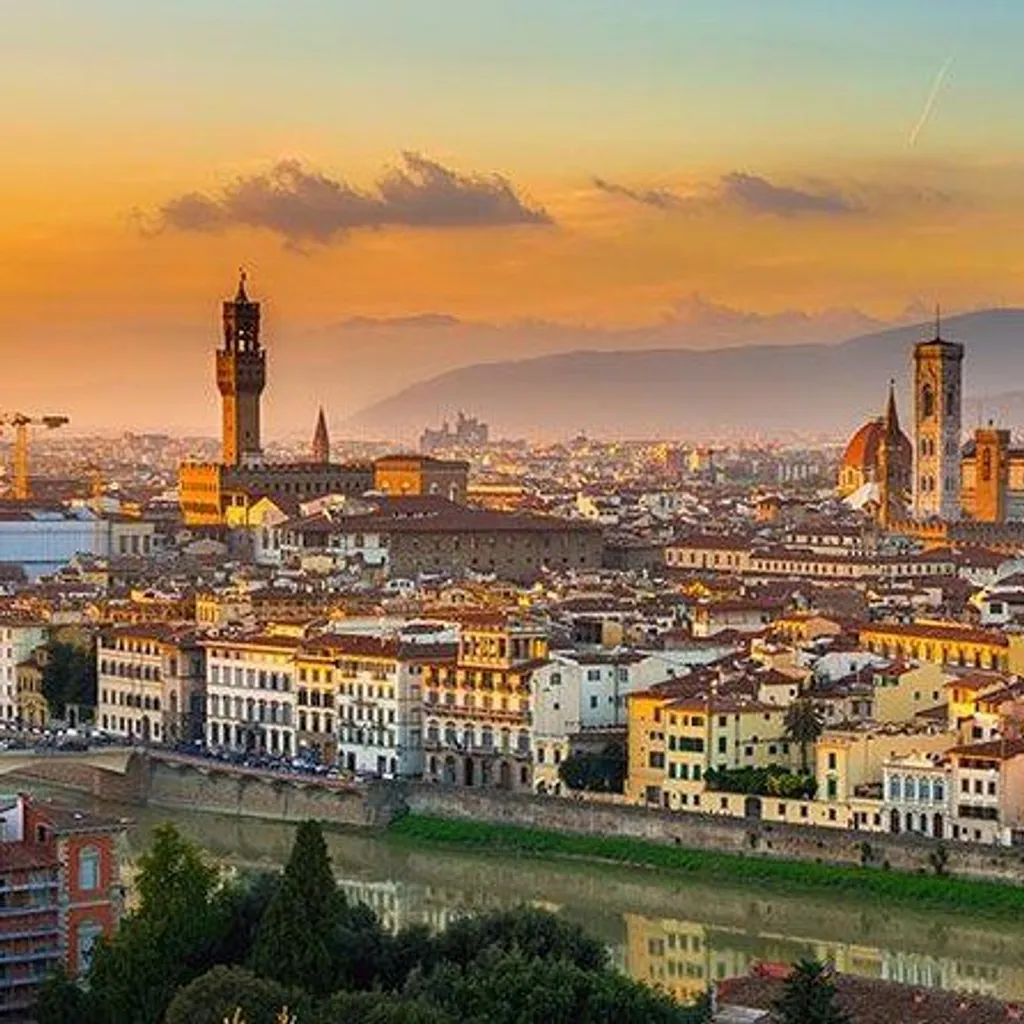 A beautiful panoramic view of Florence, Italy, captured during sunset or golden hour, featuring the iconic Duomo and Giotto's Bell Tower, with the Arno River in the foreground. The warm light bathes the historic buildings, creating a picturesque and vibrant scene.