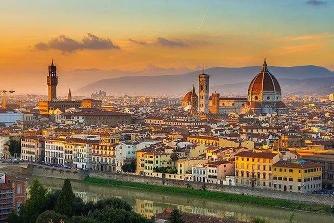 A beautiful panoramic view of Florence, Italy, captured during sunset or golden hour, featuring the iconic Duomo and Giotto's Bell Tower, with the Arno River in the foreground. The warm light bathes the historic buildings, creating a picturesque and vibrant scene.