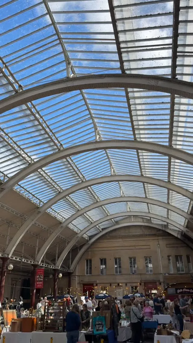 The image captures an impressive architectural glass-domed roof structure, likely from a train station or large public building. The clear blue sky is visible through the glass panels, creating a bright and airy atmosphere. The composition emphasizes the elegant curves of the metallic framework and the patterns formed by the glass.