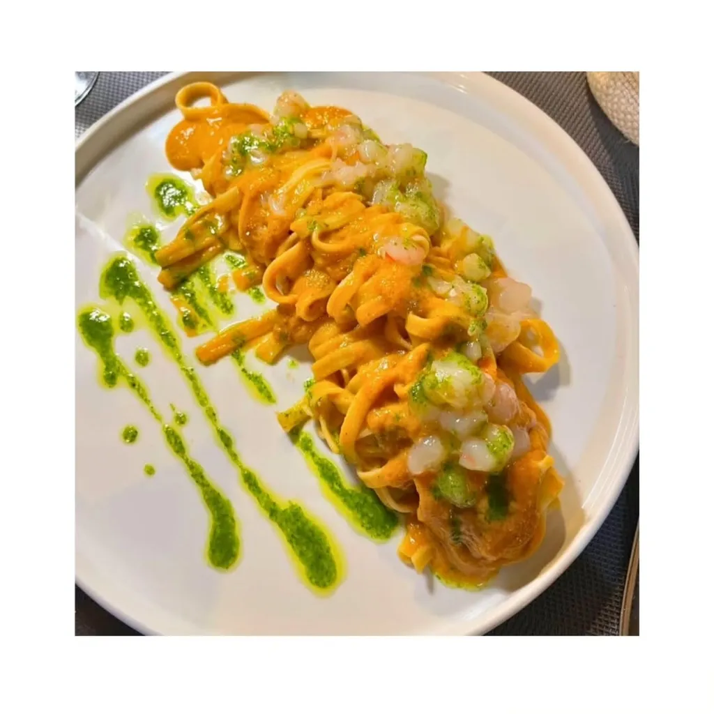 A well-composed, photo-realistic image of pasta with orange and green sauces, served on a white plate. The dish features what appears to be finely chopped ingredients or seafood on top.