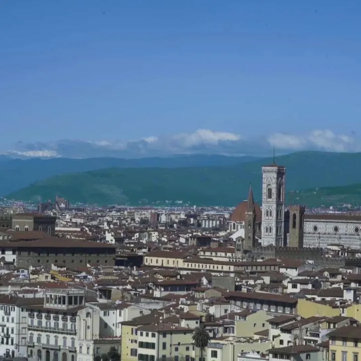 An aerial view of Florence, Italy, showcasing the city's historic architecture, including the Duomo, under a clear blue sky.