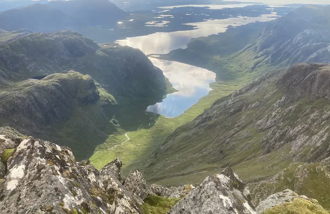 An expansive aerial view of a mountainous valley with a reflective lake. The image showcases the natural beauty of the terrain, with lush green slopes and distant bodies of water.