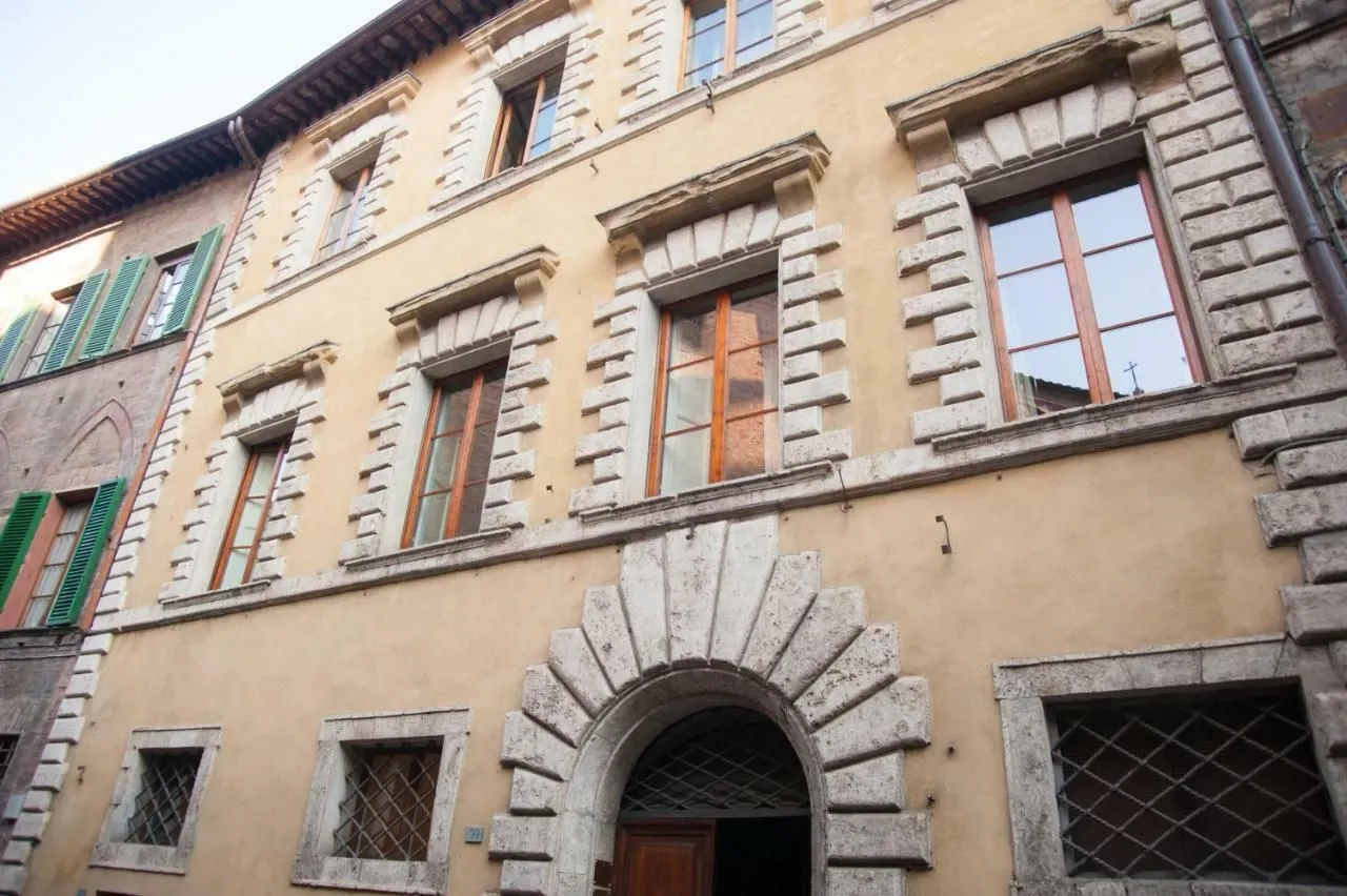 A detailed view of the exterior of an old European-style building, showcasing its yellow-beige facade, ornate stone window frames, and a large arched entrance.