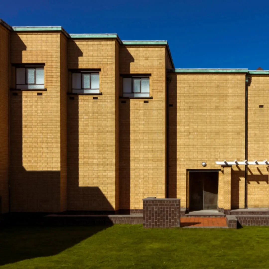 A well-composed and sharply focused photograph of a yellow brick building under a clear blue sky. The image features strong, dramatic shadows that highlight the geometric forms of the architecture and add significant visual interest.