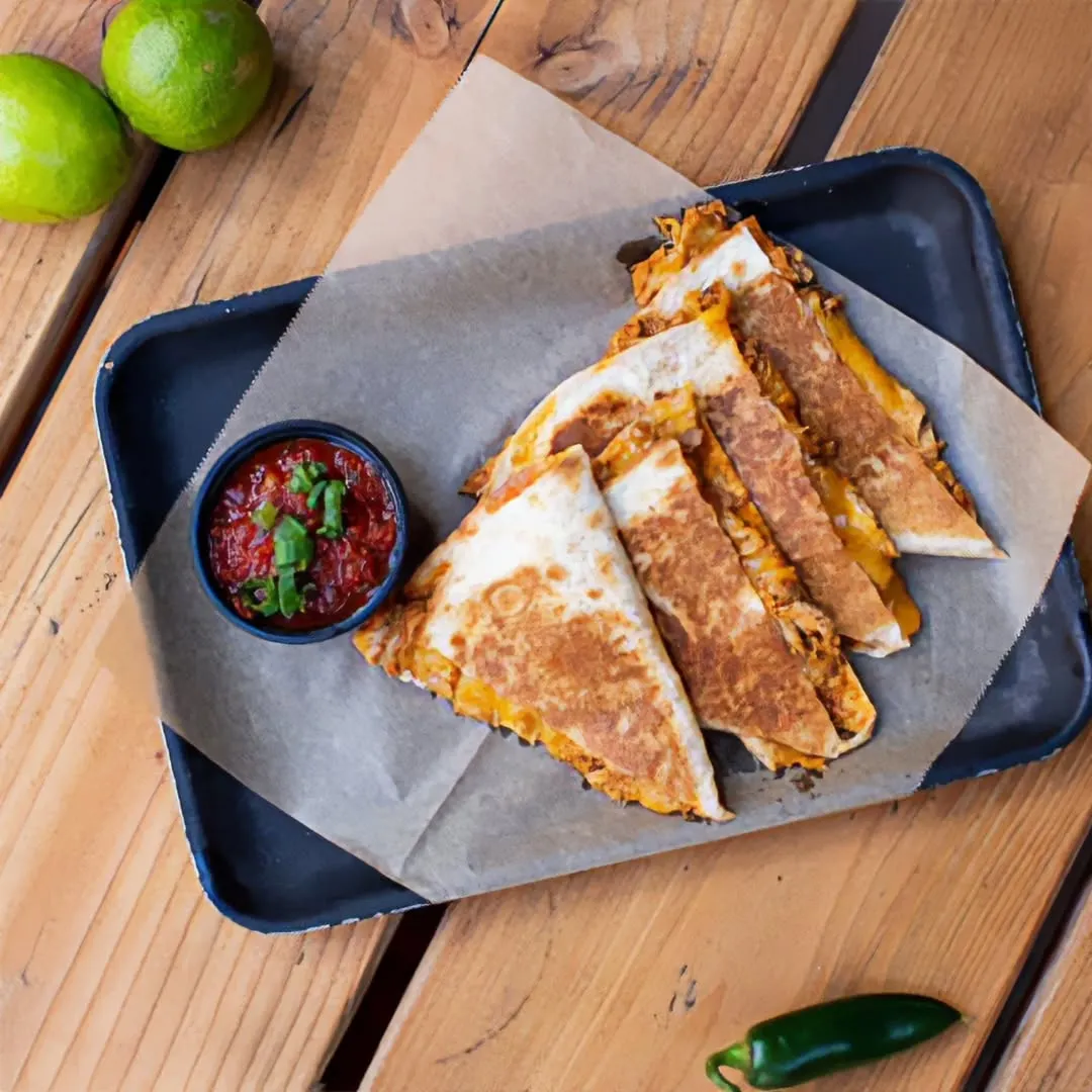 The image features a well-composed, top-down shot of several quesadilla slices served with salsa. The lighting is even and natural, highlighting the golden-brown crust of the quesadillas and the vibrant red of the salsa. The main subjects are sharp and in focus, contributing to a photo-realistic and appetizing presentation. Colors appear accurate and inviting.