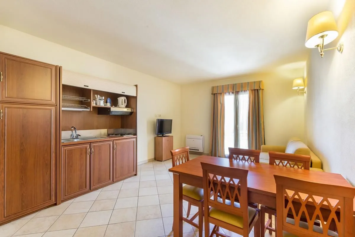 A well-lit and sharp image of a furnished room, likely a hotel apartment or rental unit, featuring a dining area and a kitchenette. The colors are accurate, and the image is photo-realistic.