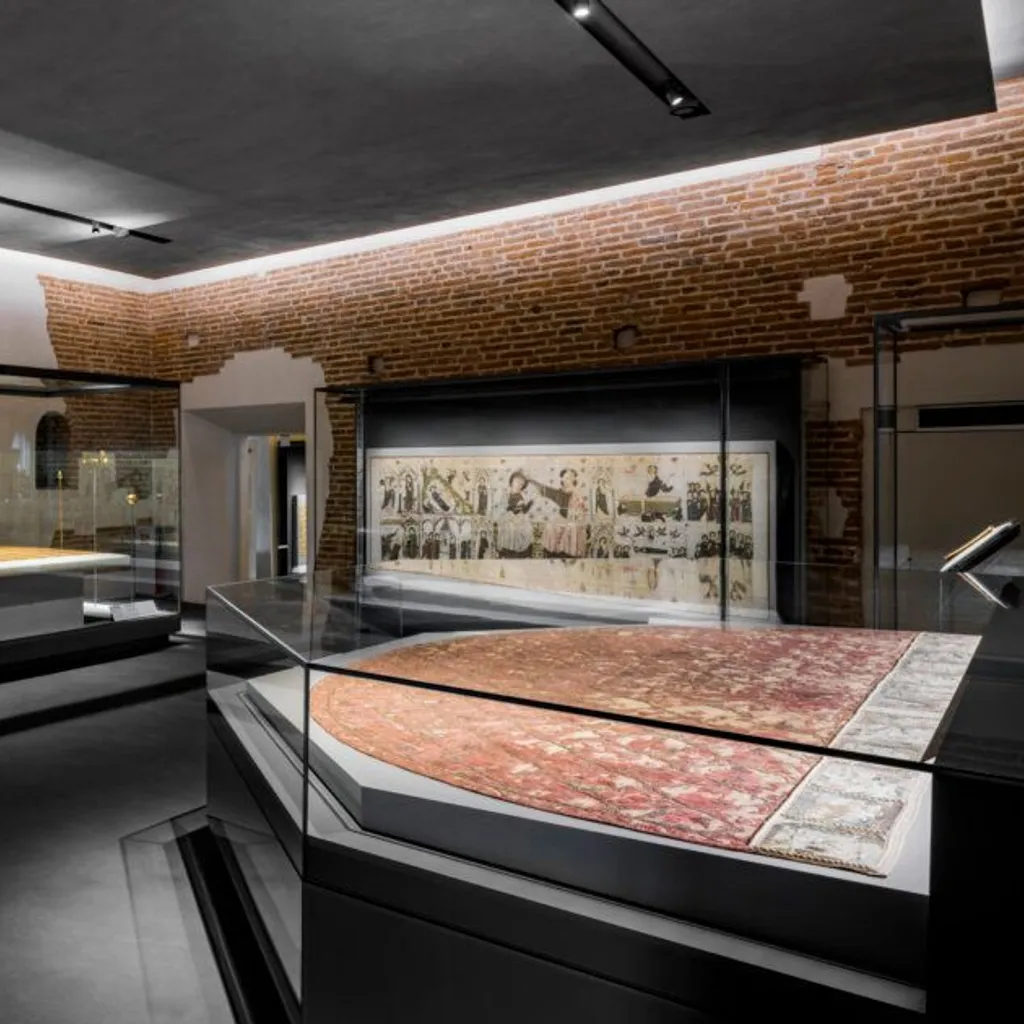 The image presents a well-composed view of a modern museum or gallery space, featuring sleek display cases housing artifacts. The contrast between the exposed brick walls and the contemporary dark floors and glass elements creates visual interest. The space is evenly and professionally lit, highlighting the exhibits without harsh shadows or overexposure.