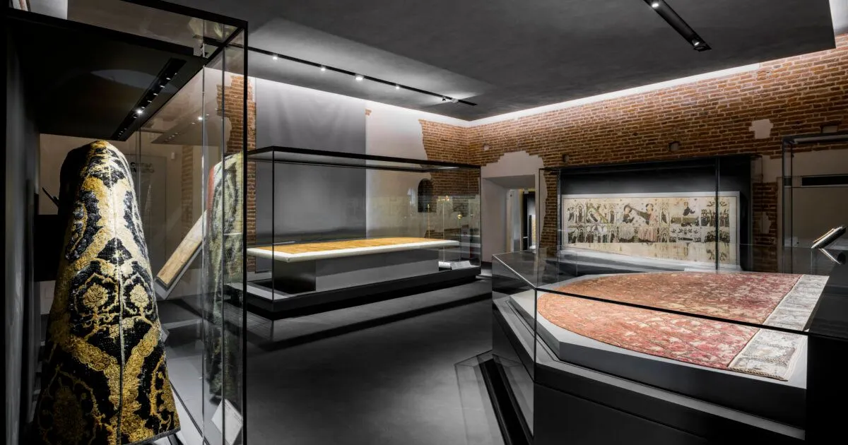 The image presents a well-composed view of a modern museum or gallery space, featuring sleek display cases housing artifacts. The contrast between the exposed brick walls and the contemporary dark floors and glass elements creates visual interest. The space is evenly and professionally lit, highlighting the exhibits without harsh shadows or overexposure.