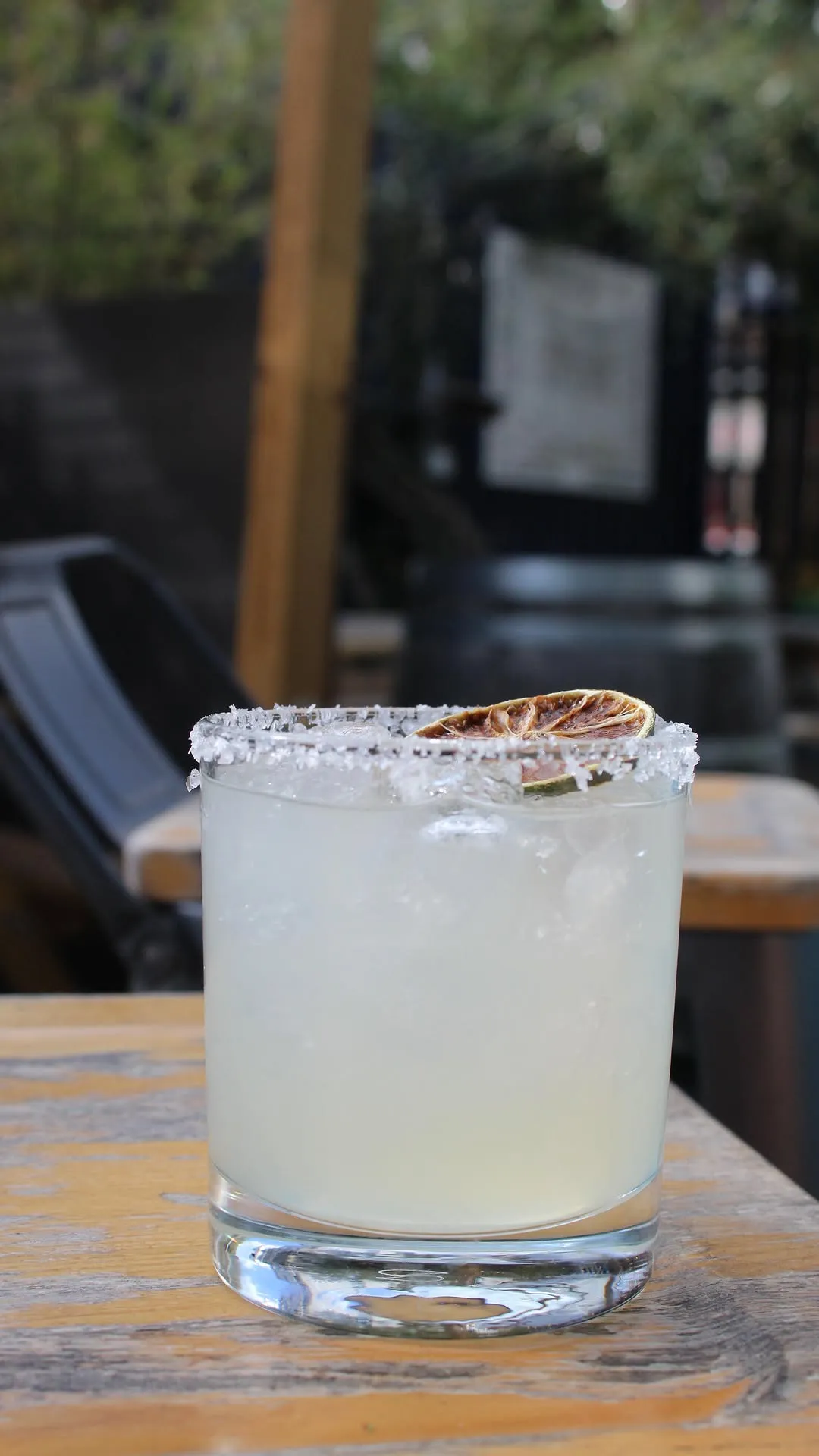 The image showcases a well-composed close-up of a refreshing cocktail, likely a margarita, with a salted rim and a dried lime slice garnish. The lighting is soft and even, highlighting the details of the drink, ice, and salt crystals. Key elements are in sharp focus, contributing to its photo-realistic quality. The colors appear natural and appealing, although the background, while blurred, contains some indistinct shapes that could be slightly more uniform.