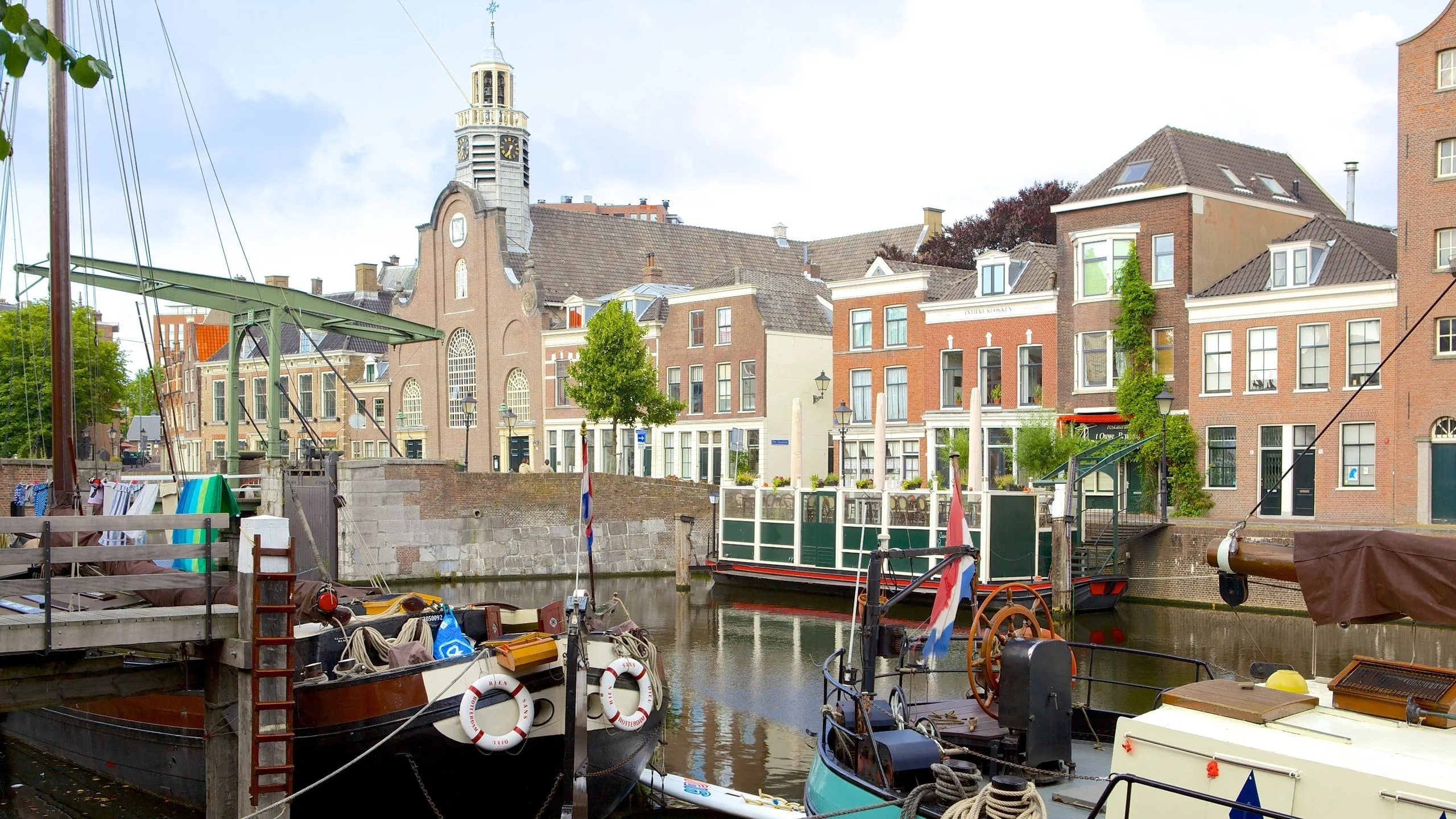 An inviting image of a canal scene in a European city, likely the Netherlands, featuring historic buildings and boats. The composition is strong, utilizing depth to showcase the architectural details and the reflections on the water. Key elements are sharp and in focus, contributing to a realistic depiction of the urban landscape.