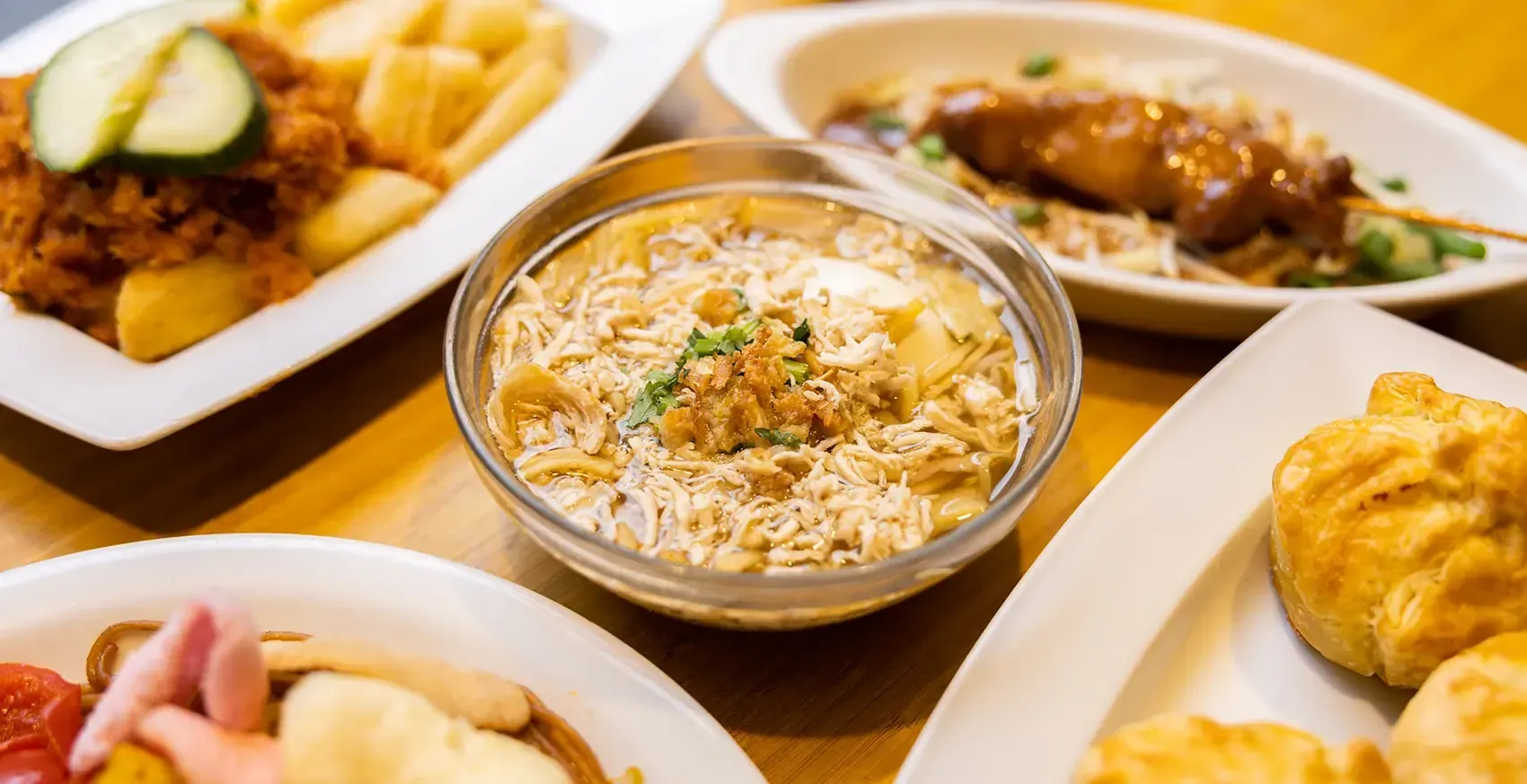 A well-composed and sharply focused close-up of a bowl of chicken and bamboo shoot soup or stew, presented on a wooden table with other out-of-focus dishes in the background.