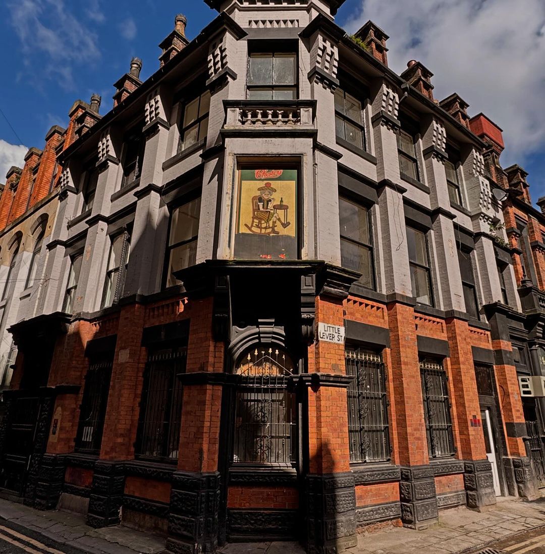 This image captures a well-composed exterior shot of a historical building, showcasing its architectural details and the surrounding urban environment. The image is well-lit, with natural sunlight illuminating the scene. The sharpness is good, allowing for clear details of the building's facade and the street sign. The colors are accurate and vibrant, capturing the warm tones of the brickwork and the cool shades of the sky. The image is photo-realistic, conveying the building's age and character. The key elements, such as the building's facade, street sign, and street itself, are in focus. The image is free from unwanted elements, such as selfies, promotional graphics, advertisements, cluttered environments, or text. The image is a great example of exterior photography, capturing the essence of the location and its historical significance.